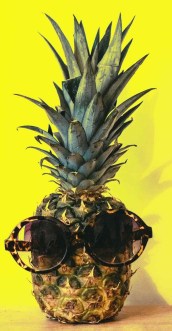 green pineapple fruit with brown framed sunglasses beside yellow surface